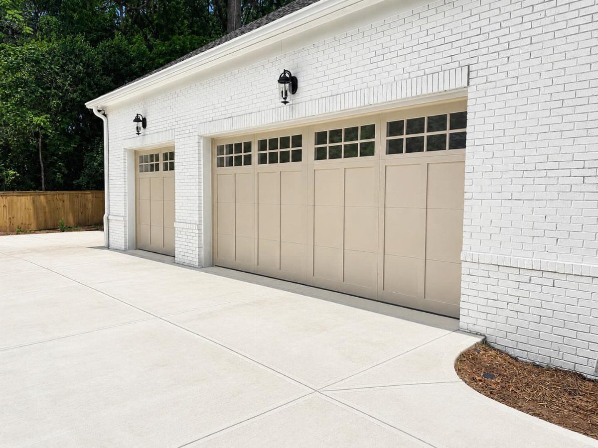 Beige garage doors with window panes on a white brick house with a concrete driveway.