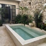 A rectangular concrete plunge pool surrounded by light pea gravel and lush tropical greenery against a stone wall.