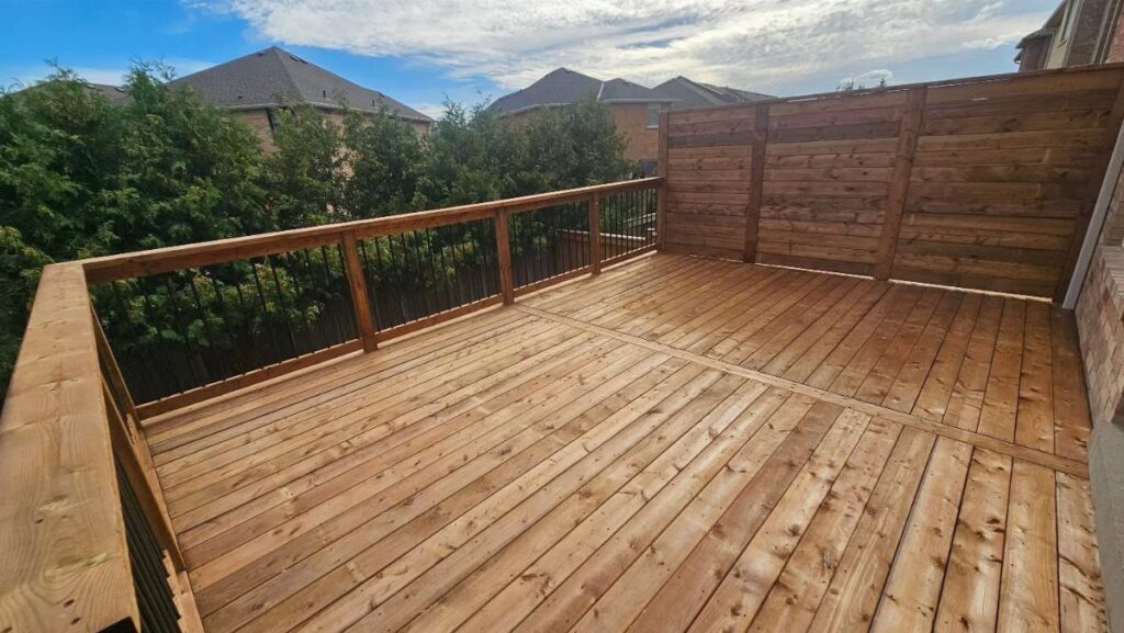 A wooden deck with a tall solid wood privacy wall and a railing overlooking green trees.