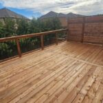 A wooden deck with a tall solid wood privacy wall and a railing overlooking green trees.