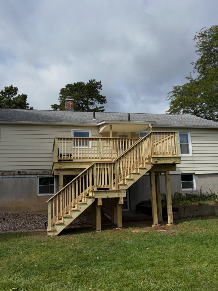Wooden deck stairs leading to a landing supported by thick wooden posts against a house.
