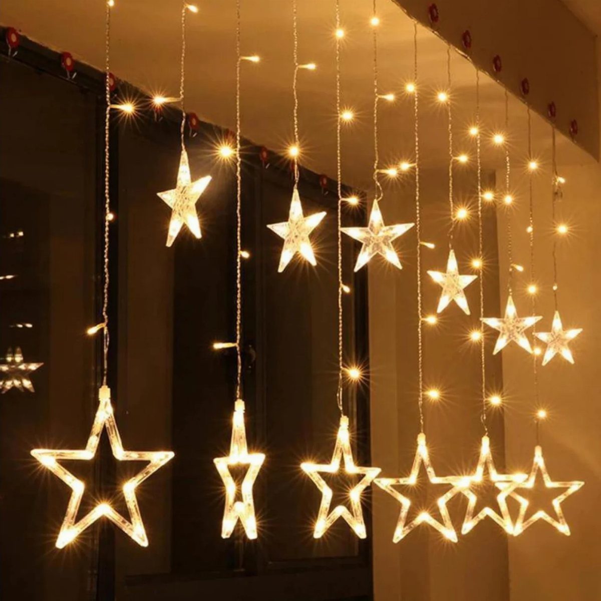 Warm white star-shaped string lights hanging vertically against a dark window backdrop.