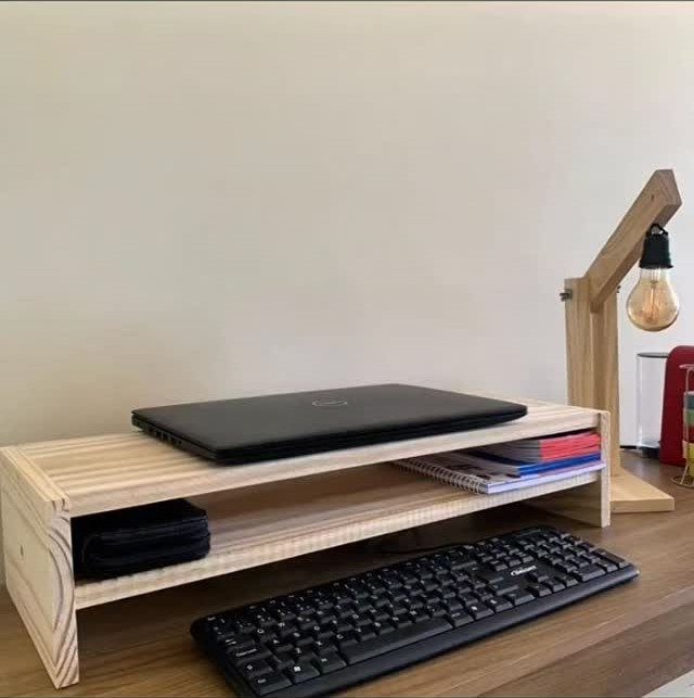 A wooden laptop stand holding a black laptop on a desk with a keyboard.