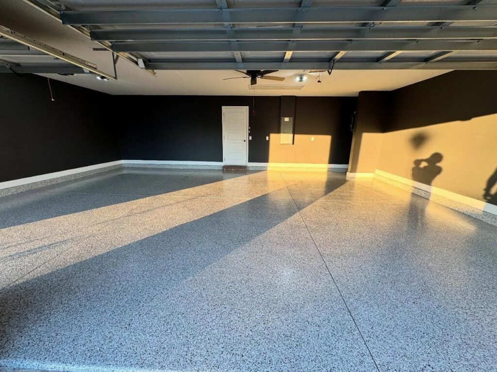 An empty garage featuring dark grey walls and a polished, speckled epoxy floor surface.