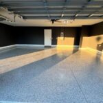 An empty garage featuring dark grey walls and a polished, speckled epoxy floor surface.