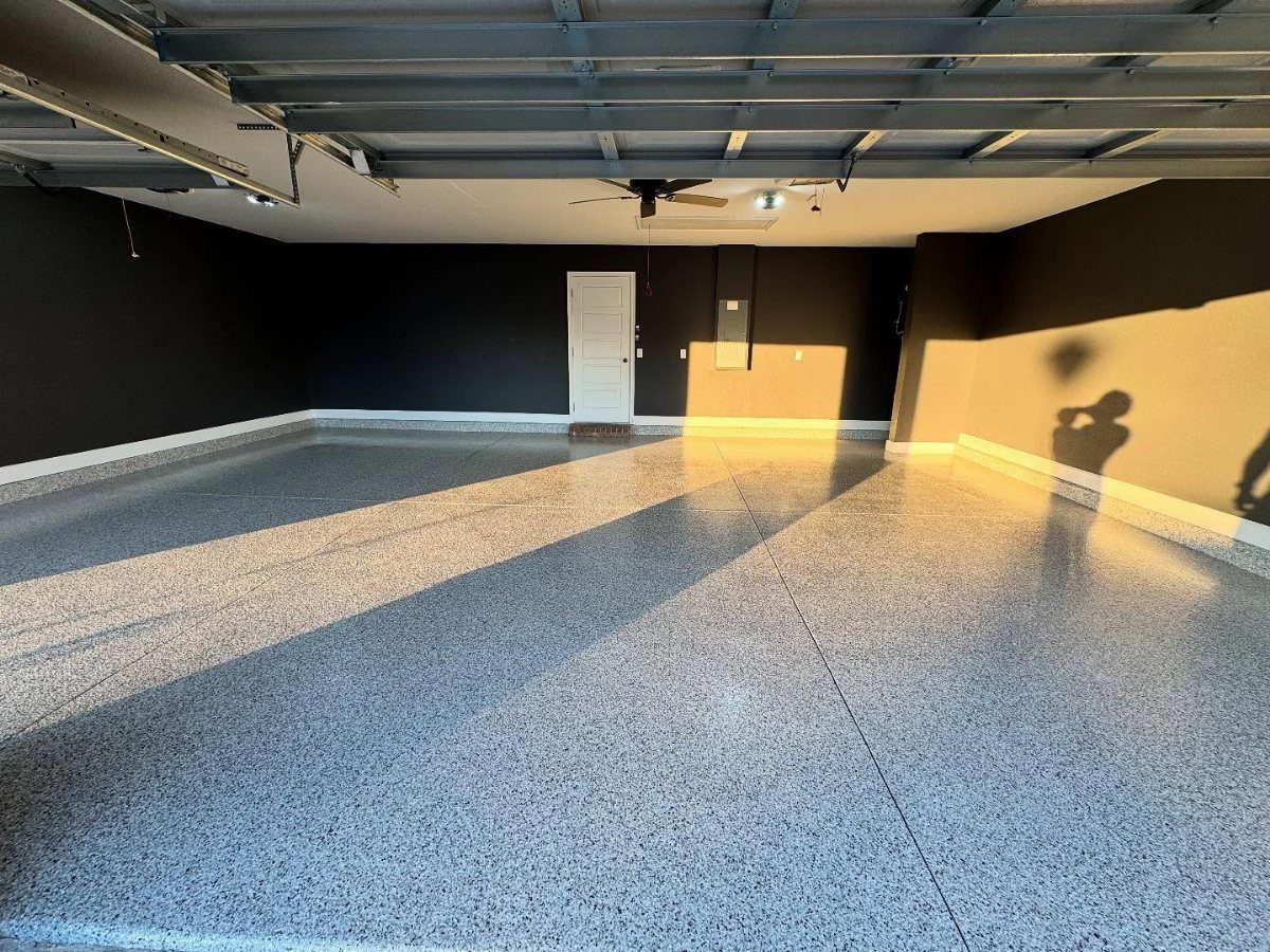 An empty garage featuring dark grey walls and a polished, speckled epoxy floor surface.