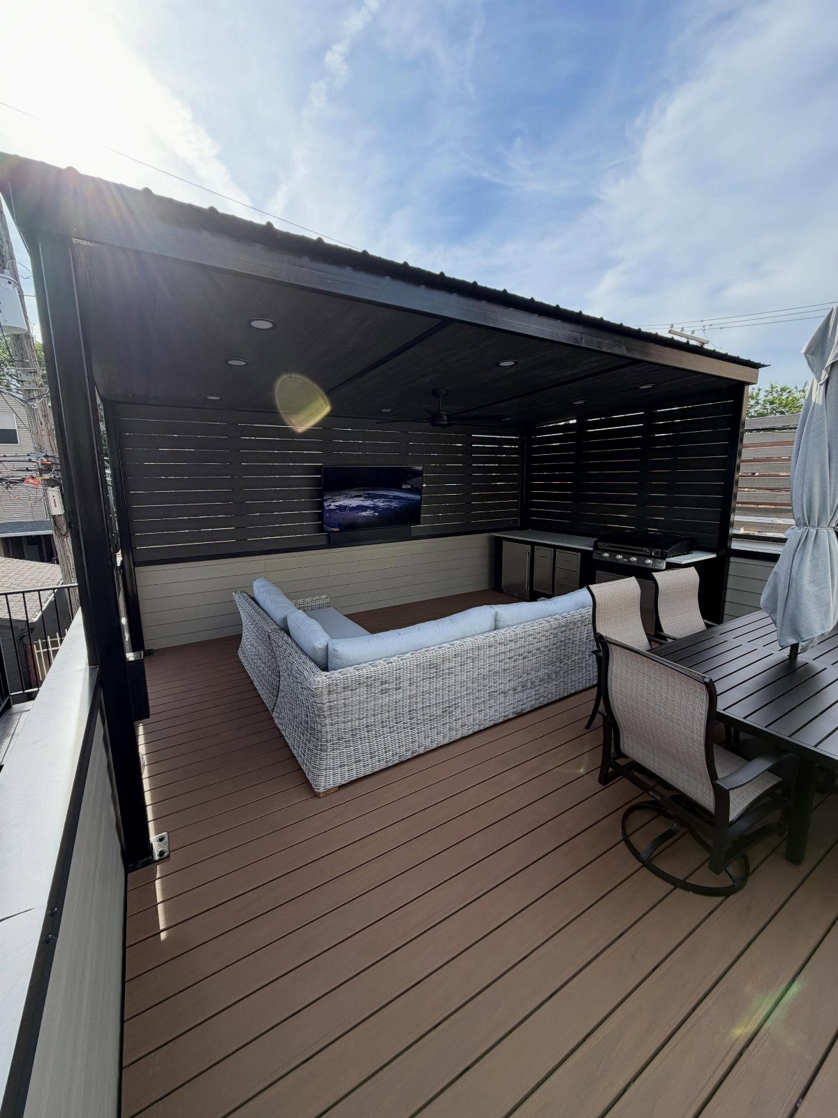 A modern rooftop deck with wicker seating, a dining set, and an outdoor kitchen area.