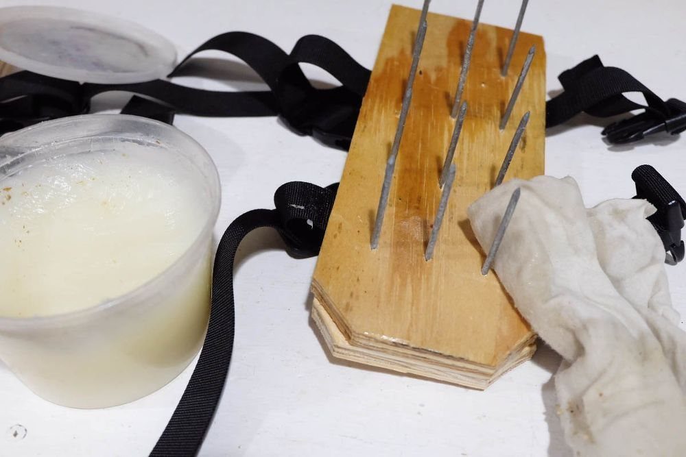 Wooden block with long metal nails and black straps lying on a white surface.